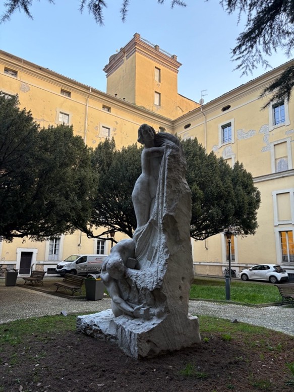 Parman yliopiston sisäpiha, puita ja patsas, jossa alaston mies on polvistunut alastoman naisen jalkojen juurelle.