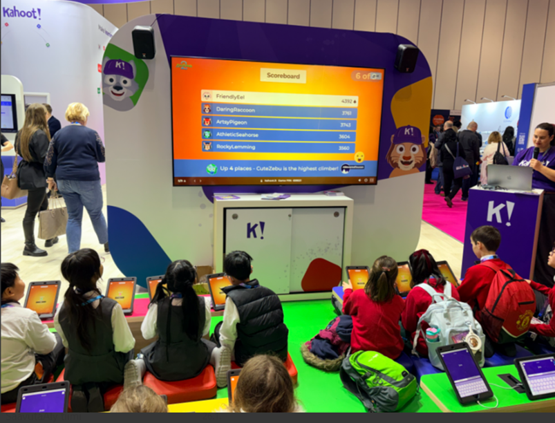 Children playing sitting on the floor with ipads, Kahoot questions showing on the big screen.