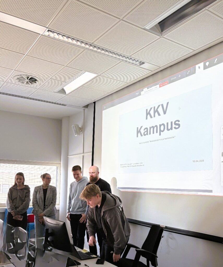 Viisi opiskelijaa seisoo valkokankaan edessä katsoen tietokoneen näyttöä. Kankaalle heijastuu KKV Kampus.